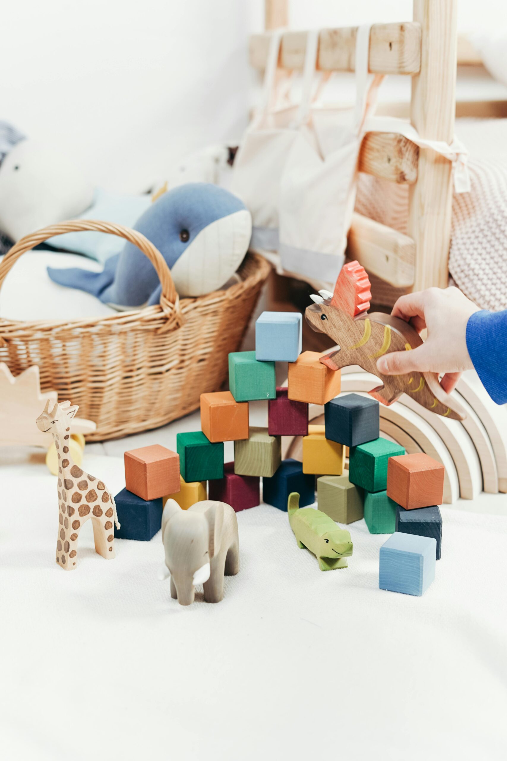 A child's hand arranges colorful wooden toys and animal figures on a playroom floor.
