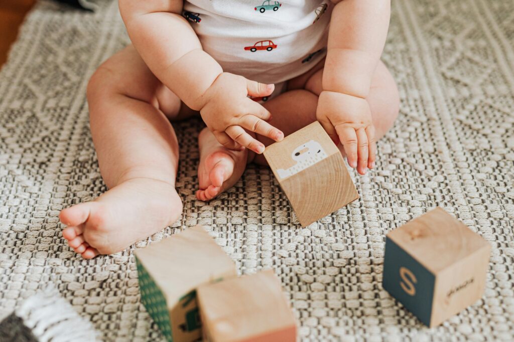 A baby sitting and playing with wooden toy blocks on a textured carpet indoors.